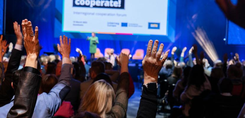 picture of an interreg event with attendees raising hands